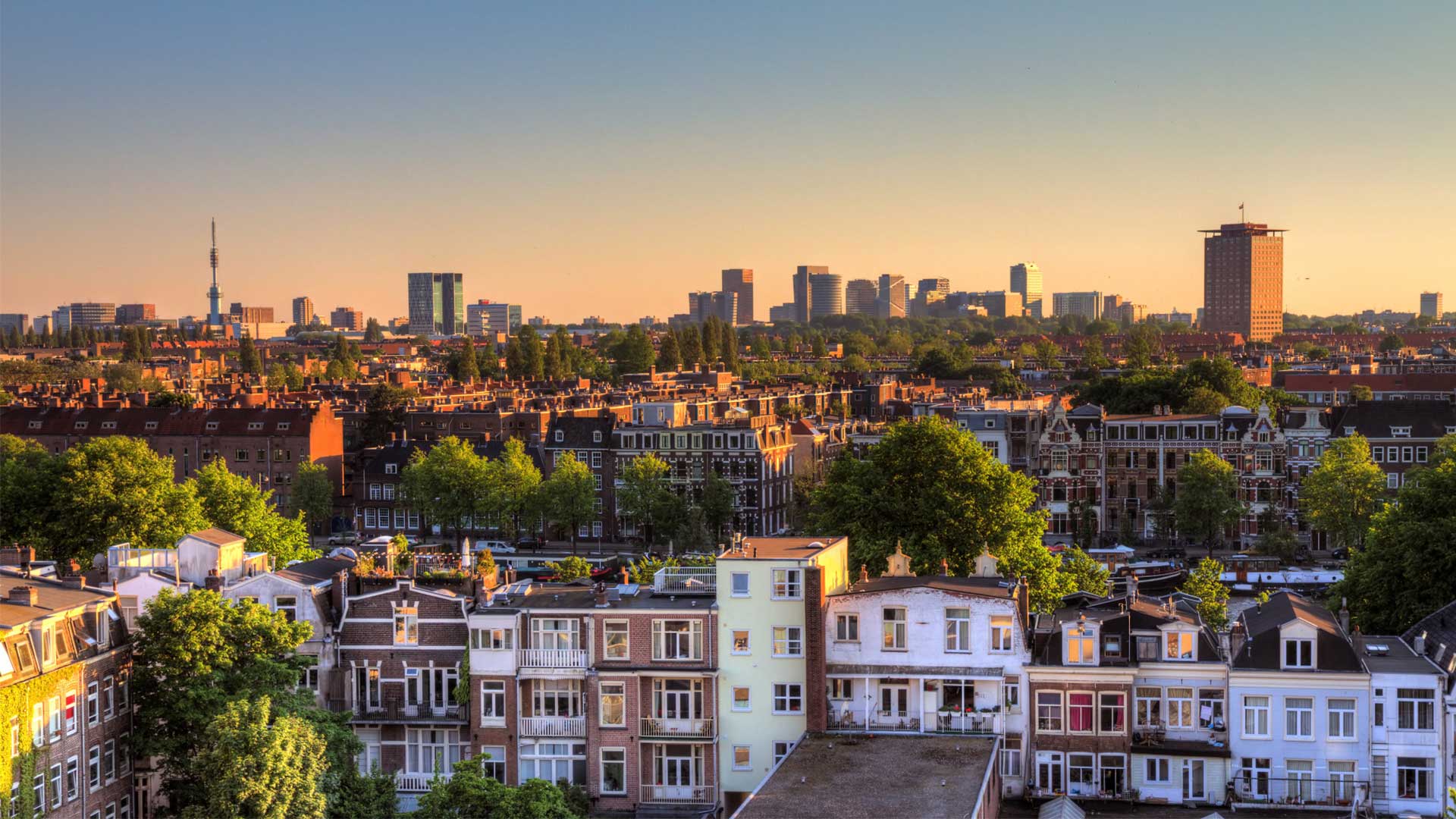 Panoramisch uitzicht op de skyline van een stad bij zonsondergang met een mix van moderne wolkenkrabbers en traditionele woonhuizen onder een gouden hemel.