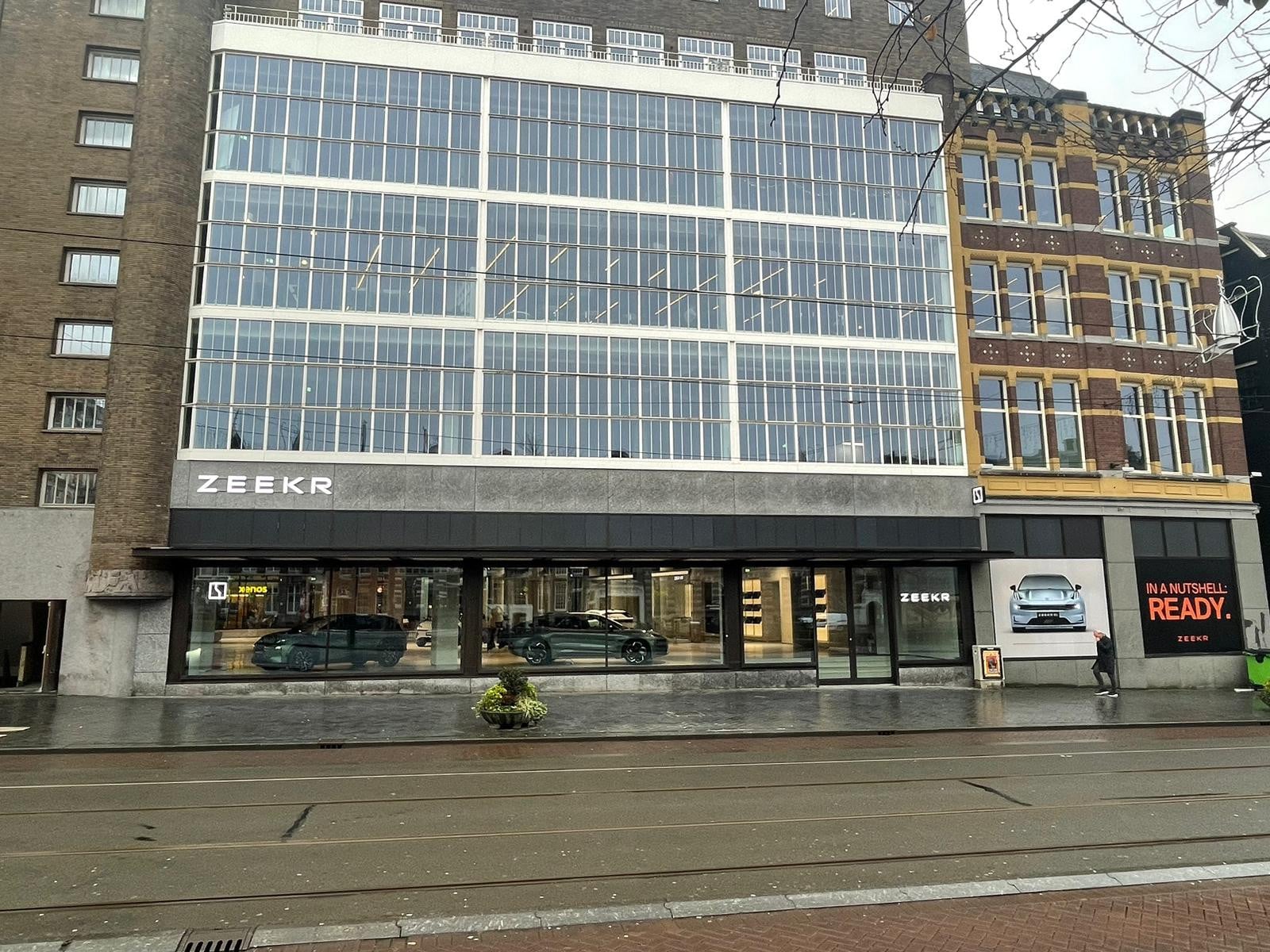 Een grote gevel van een pand met meerdere verdiepingen. De gevel van het pand bestaat veelal uit ramen/glas en in de etalage op de begane grond staan auto's in een showroom uitgestald.