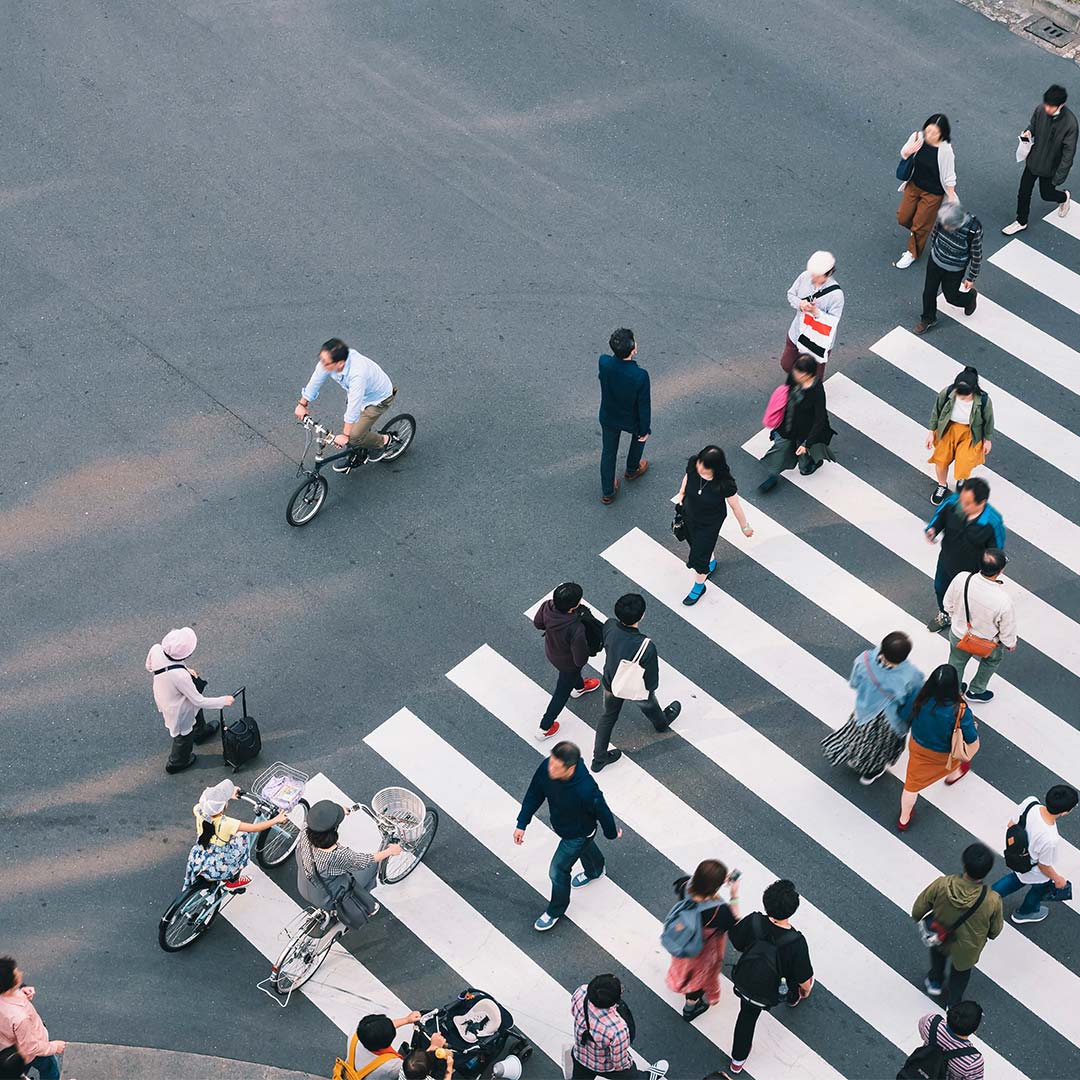 Aerial view of a busy city crosswalk with numerous pedestrians crossing in multiple directions, including a cyclist and a person pushing a cart.