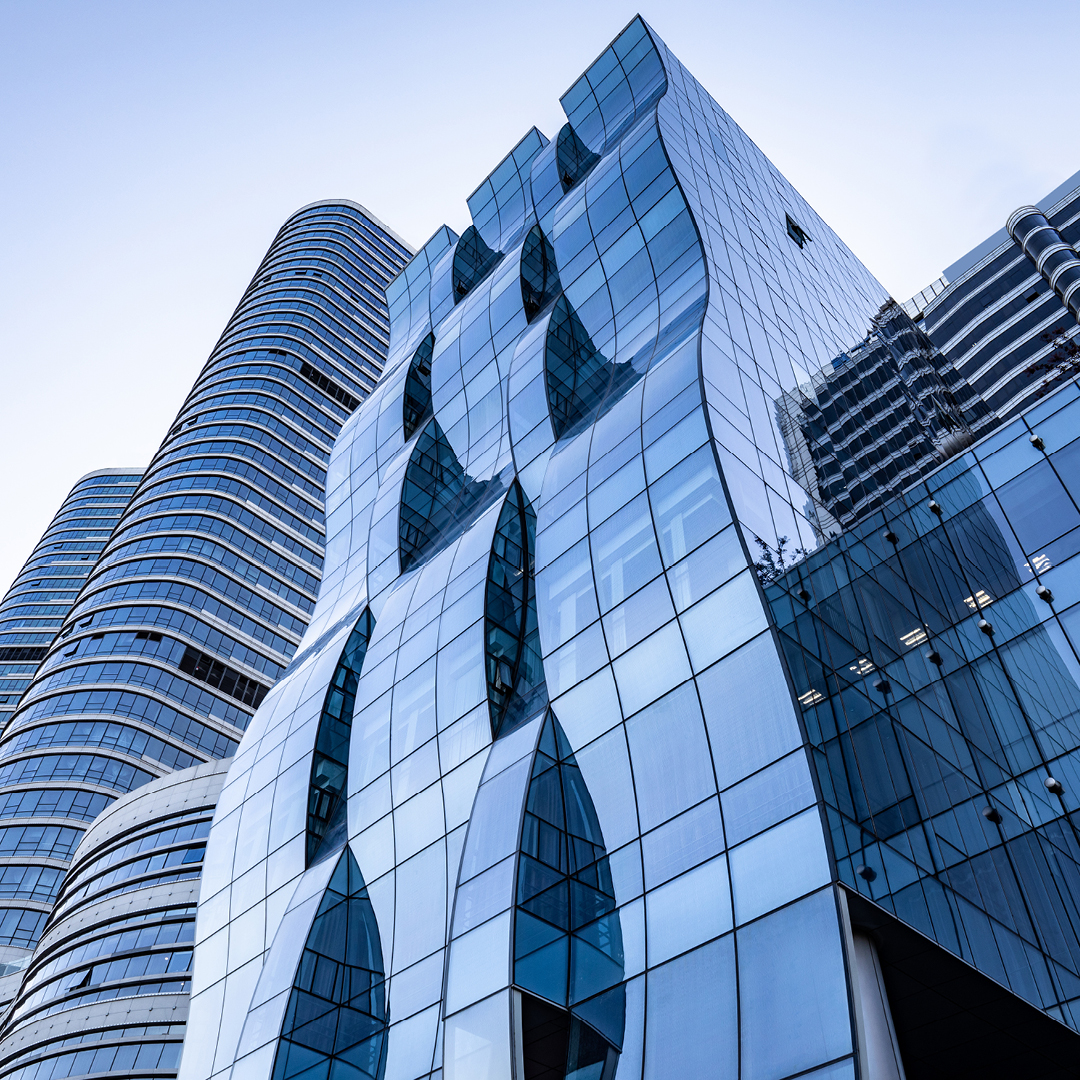 Image of a modern glass commercial building with a unique curved design, reflecting the sky and surrounding structures. Ideal for modern office space.