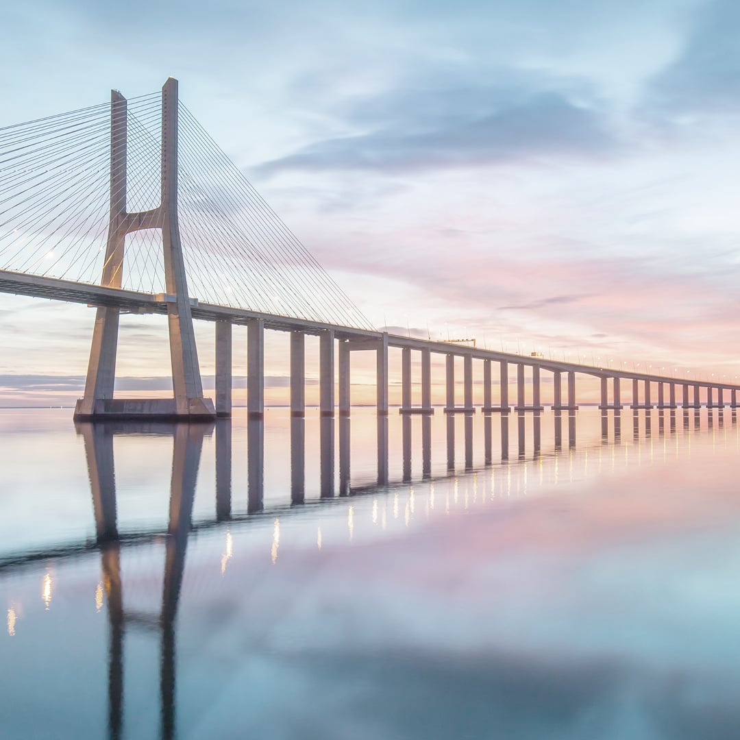 Wide view of a cable‑stayed bridge stretching across calm water at sunrise