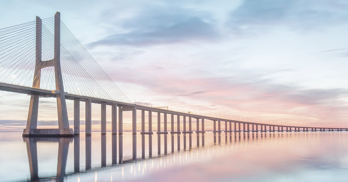 Wide view of a cable‑stayed bridge stretching across calm water at sunrise