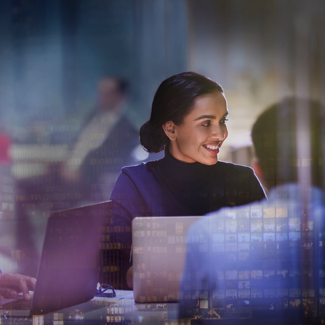 Business professionals work on laptops at night with a city skyline overlaid in the background