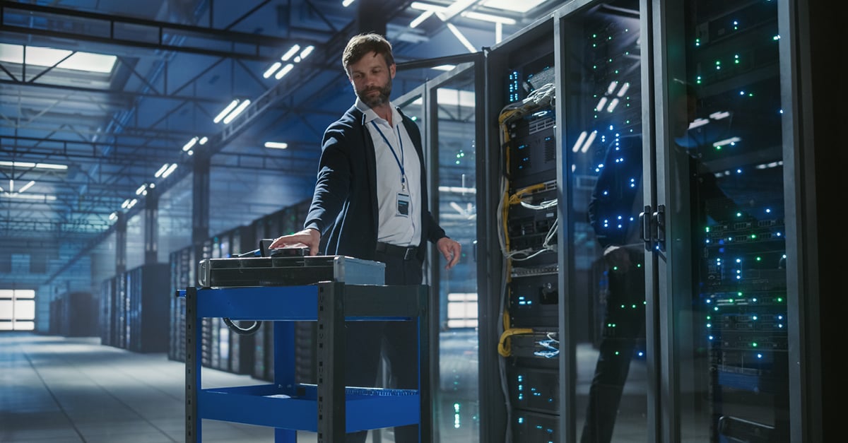 CBRE data center technician using a service cart to manage server rack equipment with illuminated networking hardware in a commercial facility.