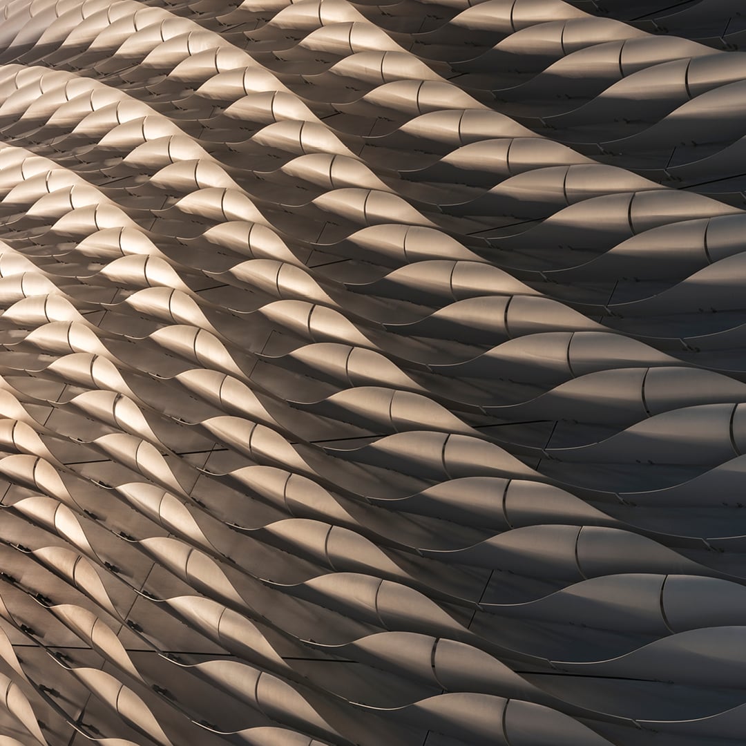 Close-up of a modern building facade with a repeating wavy, scalloped metal panel pattern