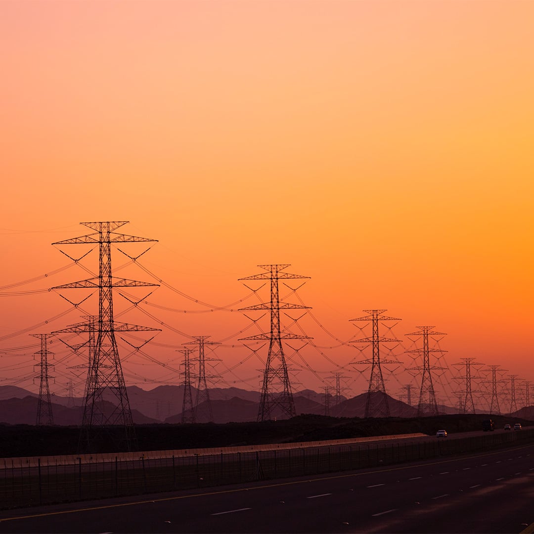 Silhouette of electrical transmission towers along a highway at sunset with a vivid orange sky