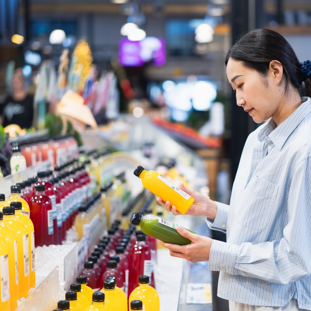 A customer compares two beverage bottles in a vibrant Australian shopping centre, reflecting consumer choices and retail trends for 2026.