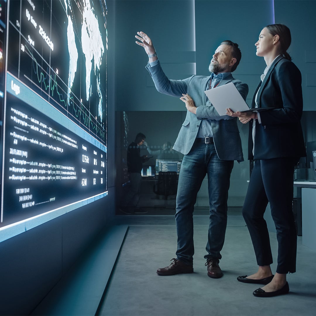 Two professionals analyzing global data on a large interactive digital wall in a modern operations room.