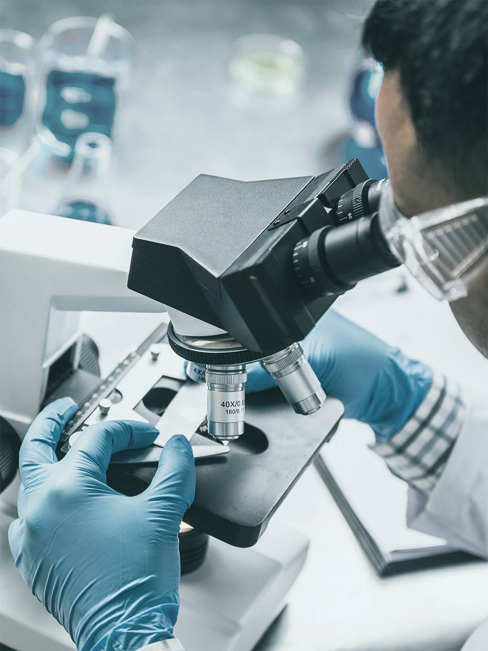 Scientist in full personal protective equipment looking at slides through a microscope