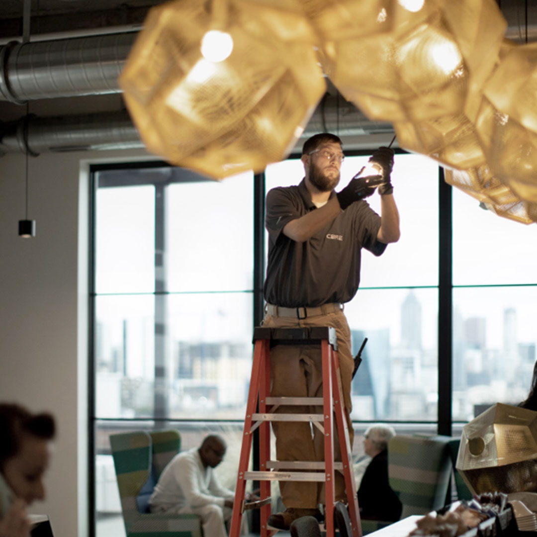facilities management employee on a ladder making repairs