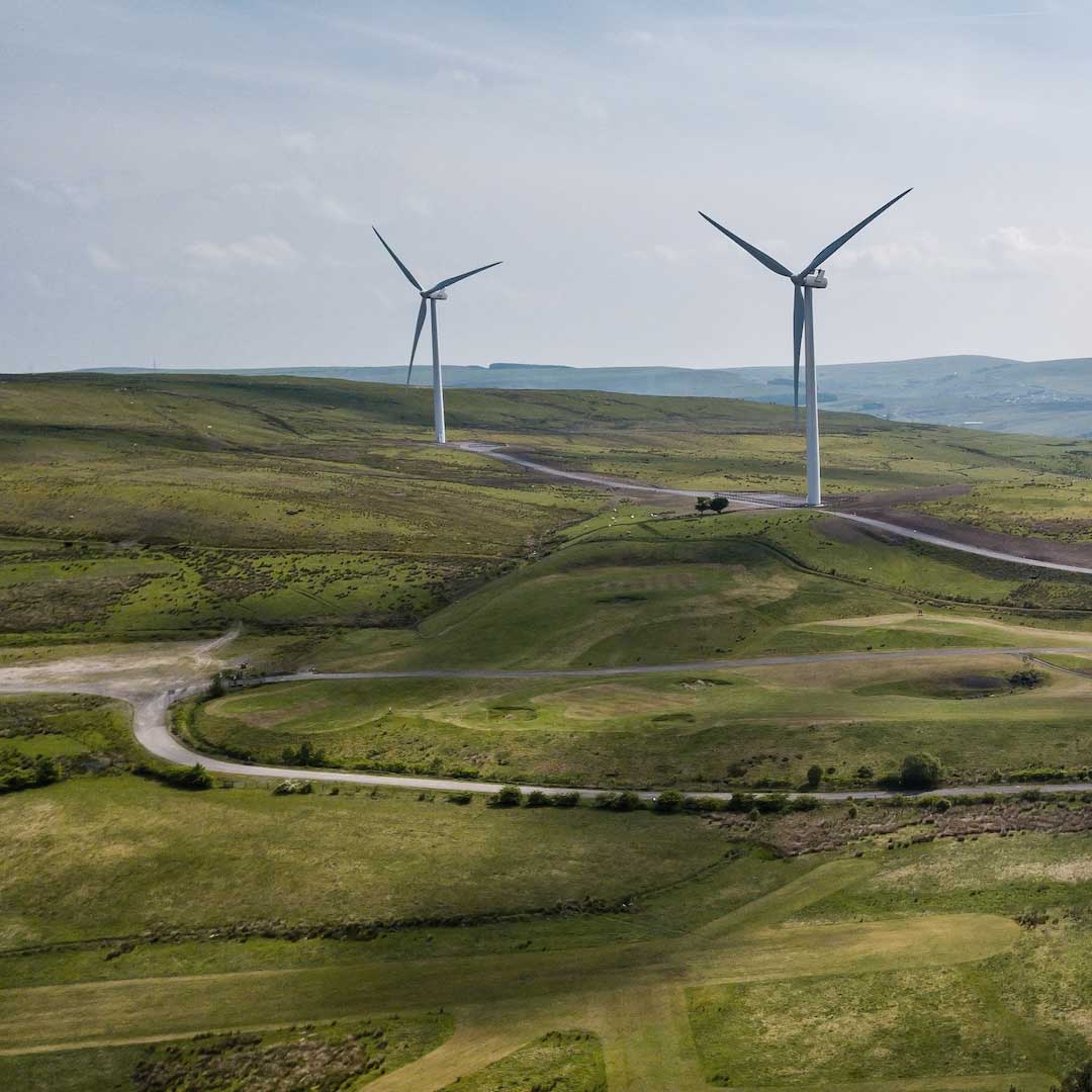 An outdoor shot of wind turbines on a hill with green grass