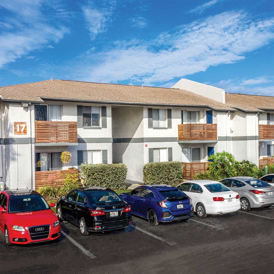 Exterior of two story apartment complex with cars parking in a parking lot in front