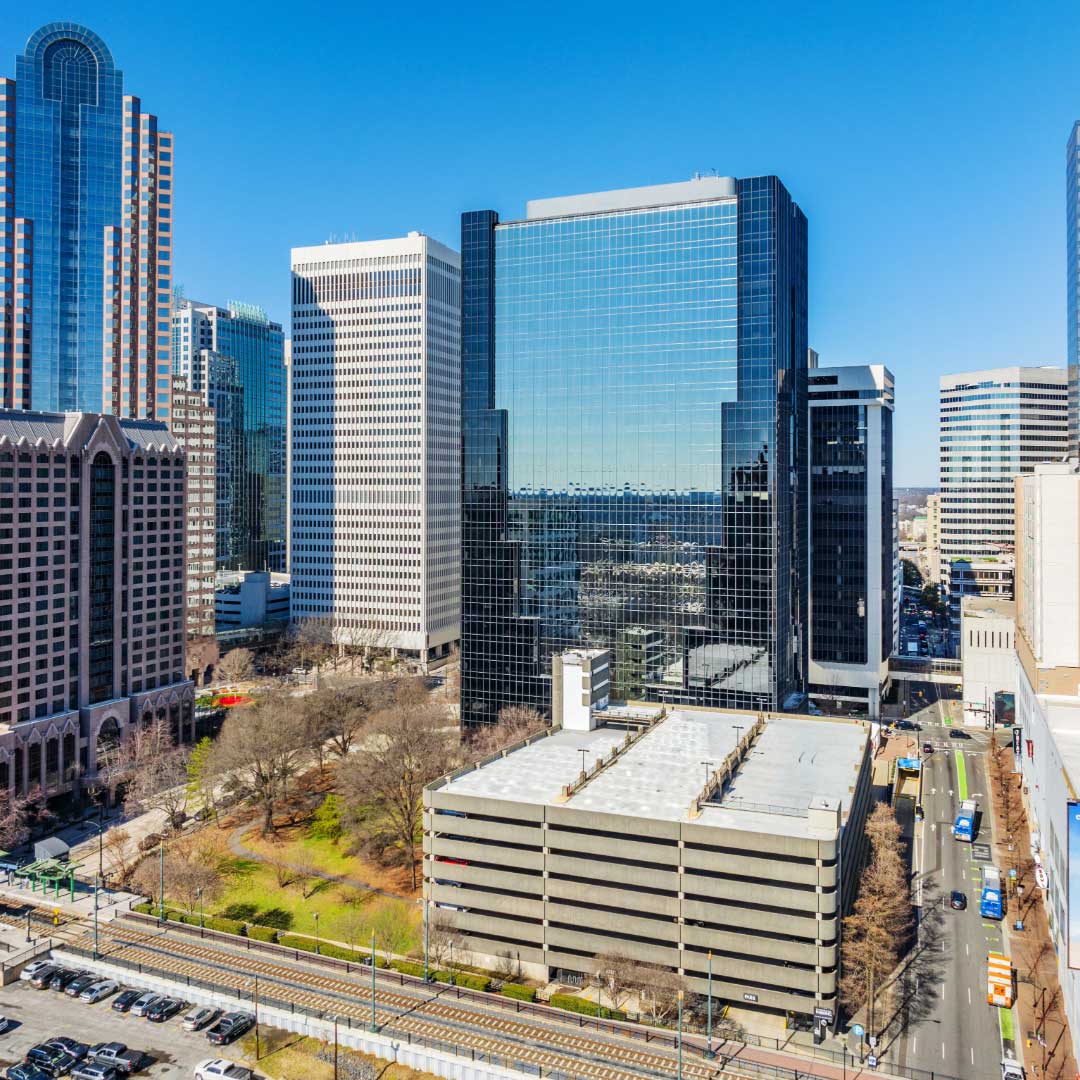Cityscape with tall glass office buildings including Charlotte Plaza, a parking garage, and a light rail track under a clear blue sky.