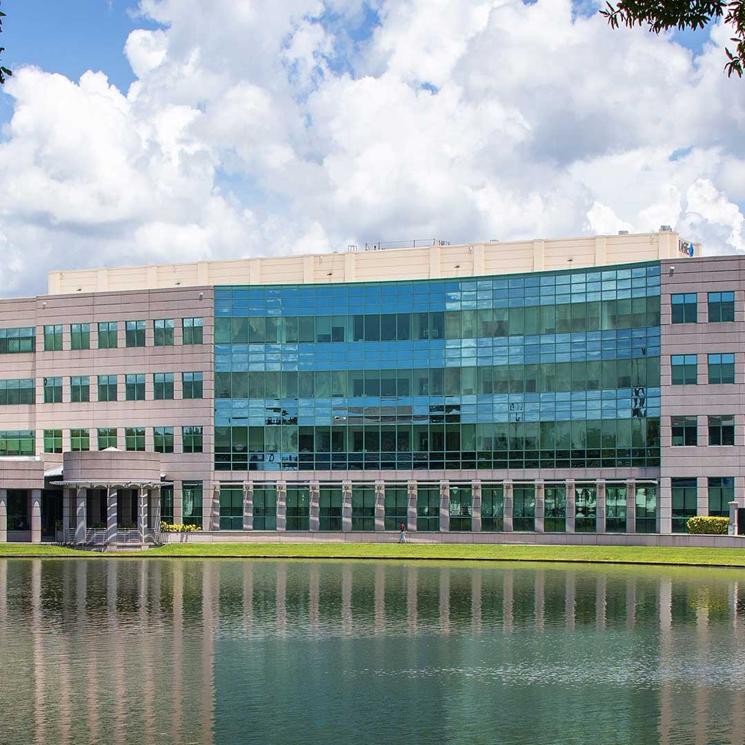 Exterior of office building with glass panels down the middle and pond in front