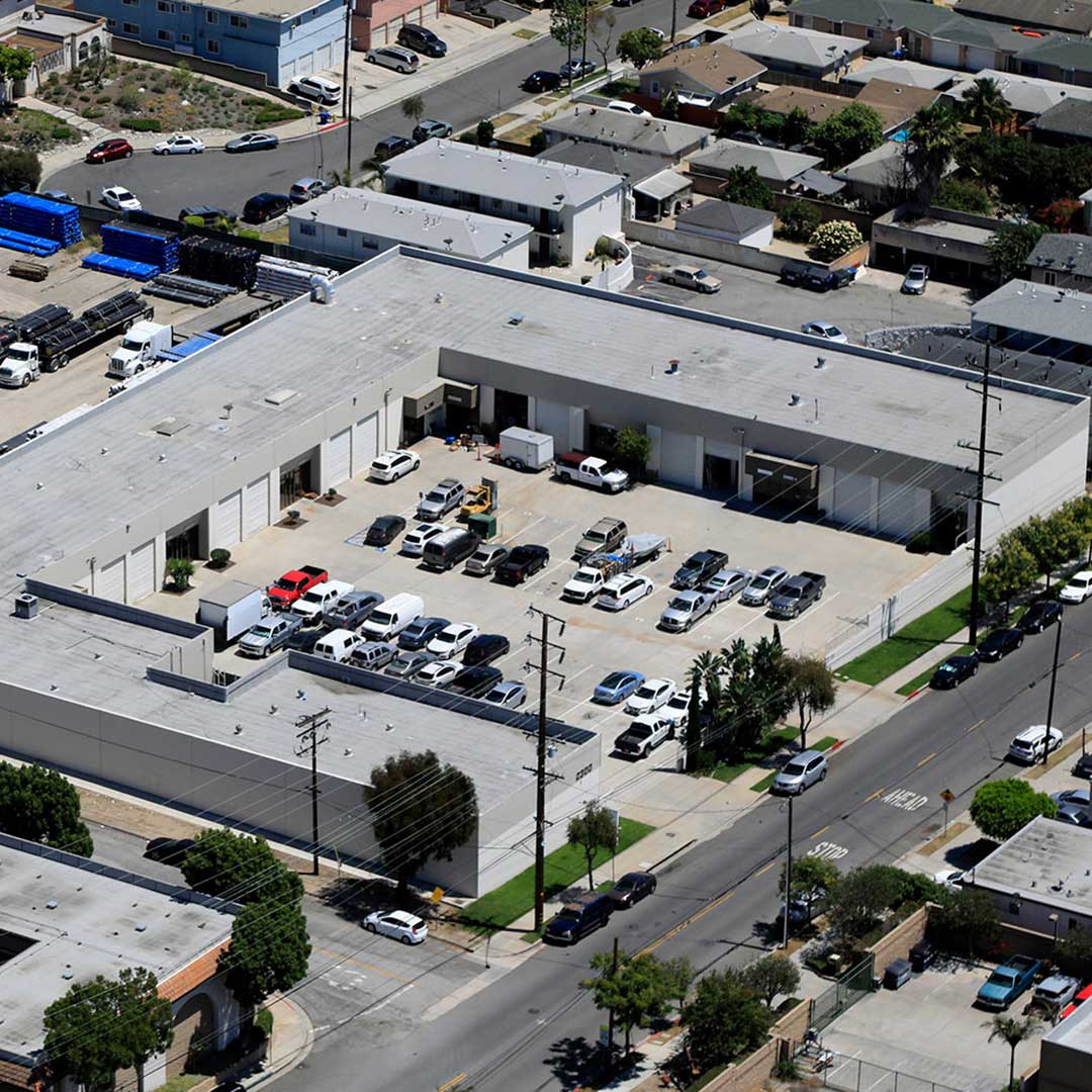 Aerial view of an industrial building with parked vehicles and surrounding streets in a commercial area.