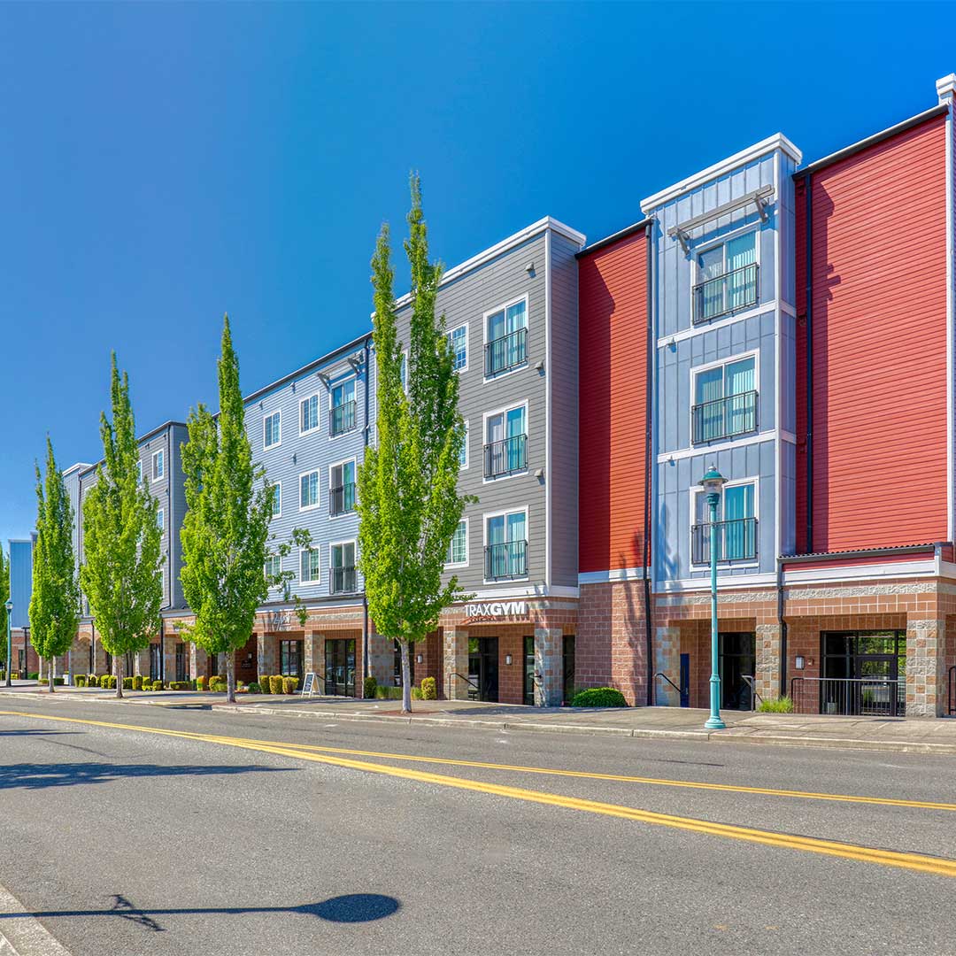Red and grey exterior of three story apartment building with ground floor retail.