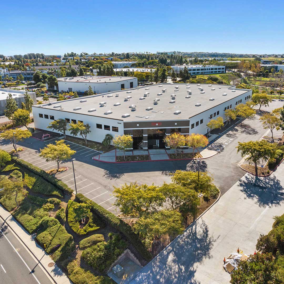 Aerial view of a large white industrial building with surrounding trees and parking lot.