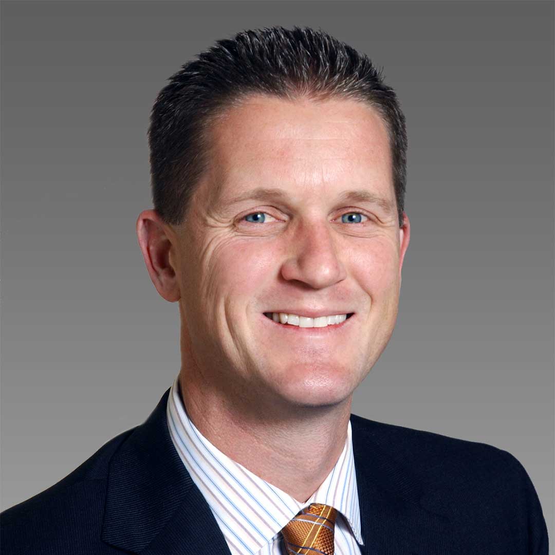 Andy Schmitt wearing a black suit jack, striped collared shirt and red and gold tie.