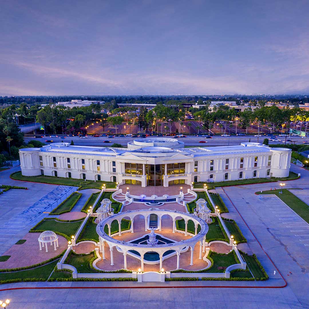 Aerial view of a white neoclassical building with landscaped gardens and decorative arches at dusk.