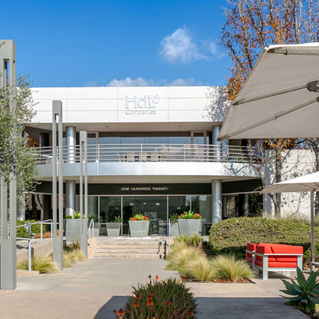 HdL Companies office building with white facade, glass entrance, planters, and landscaped walkway under blue sky.