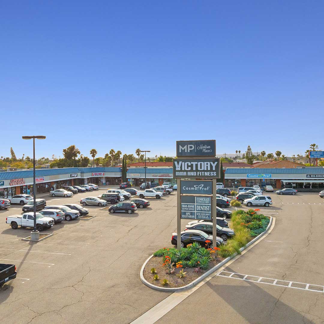 Shopping center parking lot with cars, landscaped area, and sign for Victory MMA and Fitness.