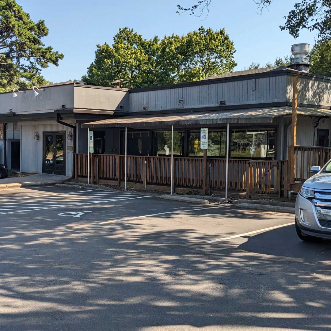 Exterior view of Longleaf Swine's future restaurant space in Greystone Village, showing a single-story building with a fenced patio and accessible parking signs.