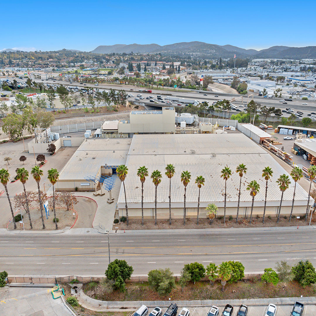 Aerial view of an industrial building with palm trees along the street and highways in the background.