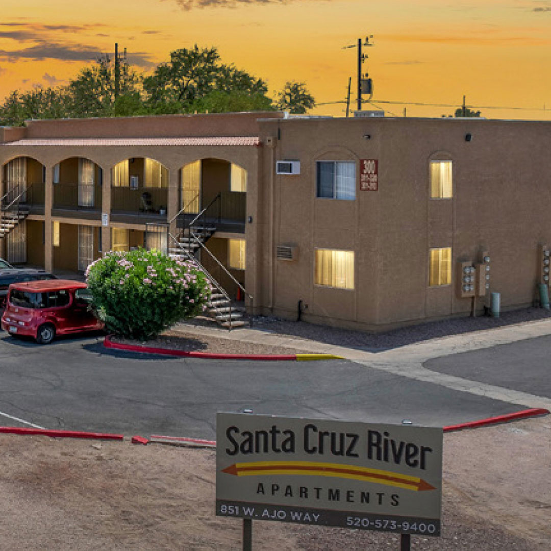 Santa Cruz River Apartments building at sunset with sign in front and parked car nearby.