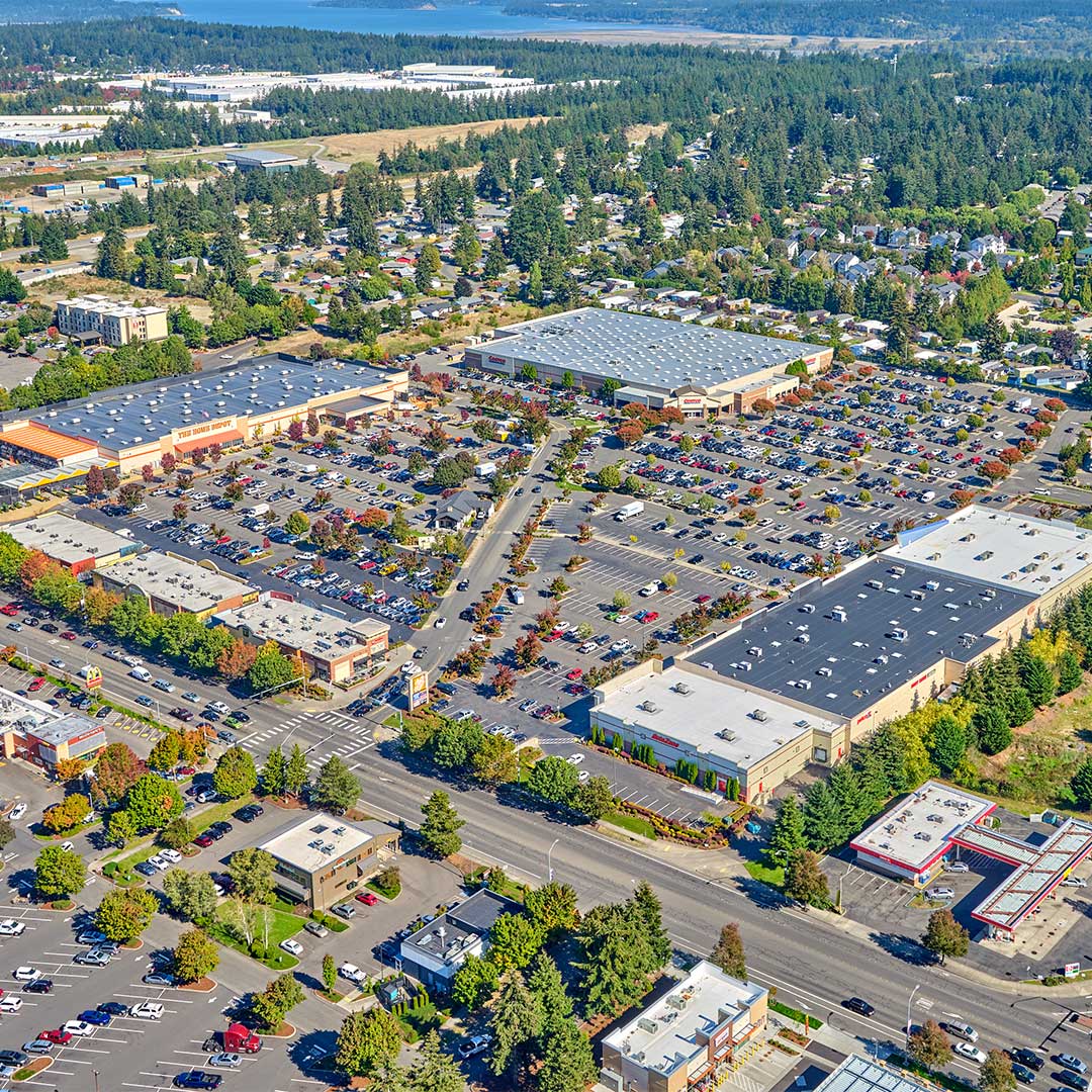 Aerial of shopping center with three buildings on the perimeter and parking lot in the center.