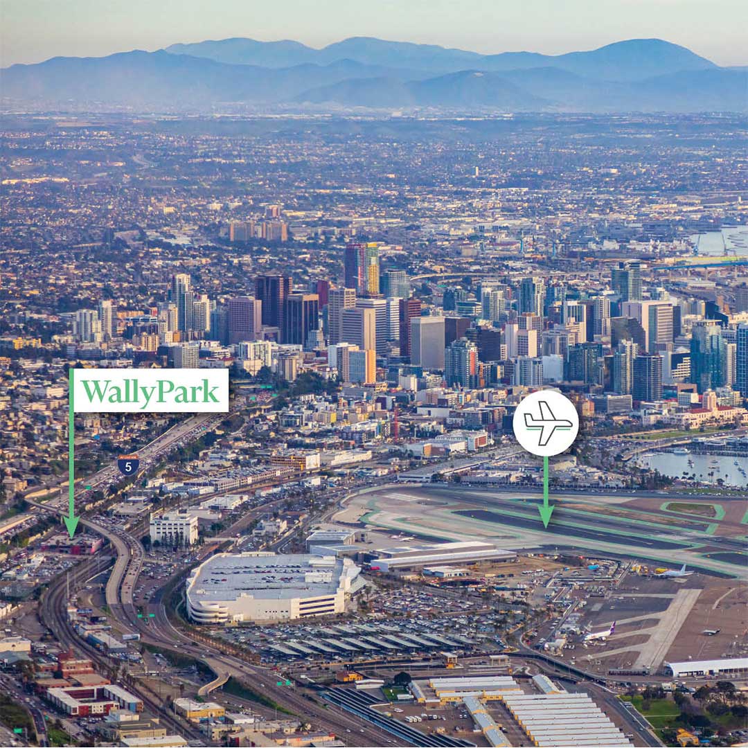 Aerial view of a city with a downtown area featuring numerous tall buildings. In the foreground, there is an airport with runways and various airport facilities. Two labeled points of interest are marked: "WallyPark" near the left side of the image and an airplane icon indicating the location of the airport on the right side. The background includes mountains under a clear sky.