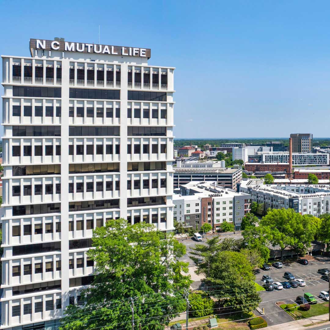Mutual Tower building with 'N C Mutual Life' sign on top, surrounded by other buildings and greenery.