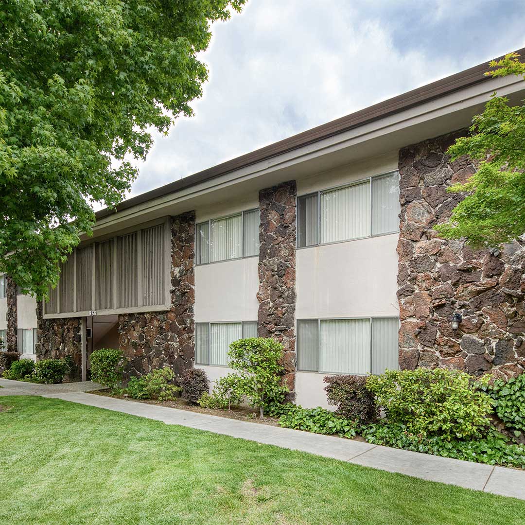 Stone exterior of Howe Manor Apartments with bushes and grass