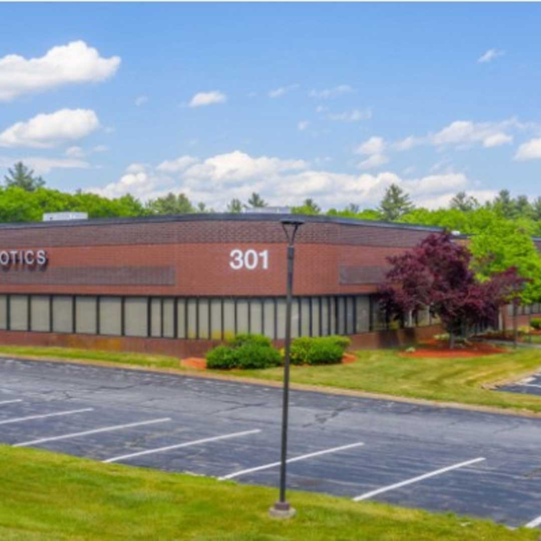 xterior view of a Locus Robotics commercial building with brick facade, parking lot, and landscaped surroundings at 301 Ballardvale Street.