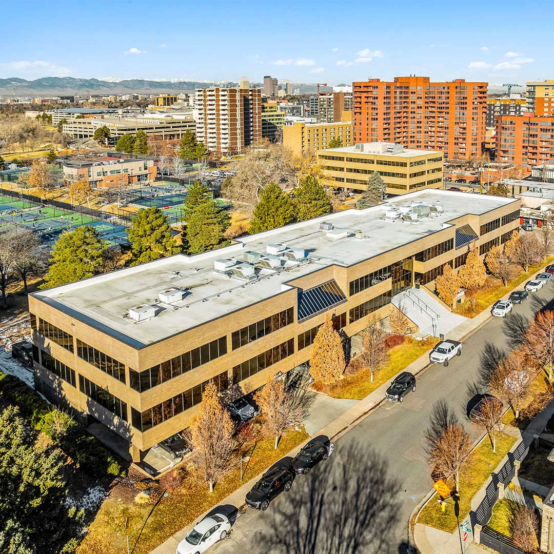 Aerial view of Cherry Creek Medical Pavilion with modern office building, nearby tennis courts, tree-lined streets, and Denver city skyline.