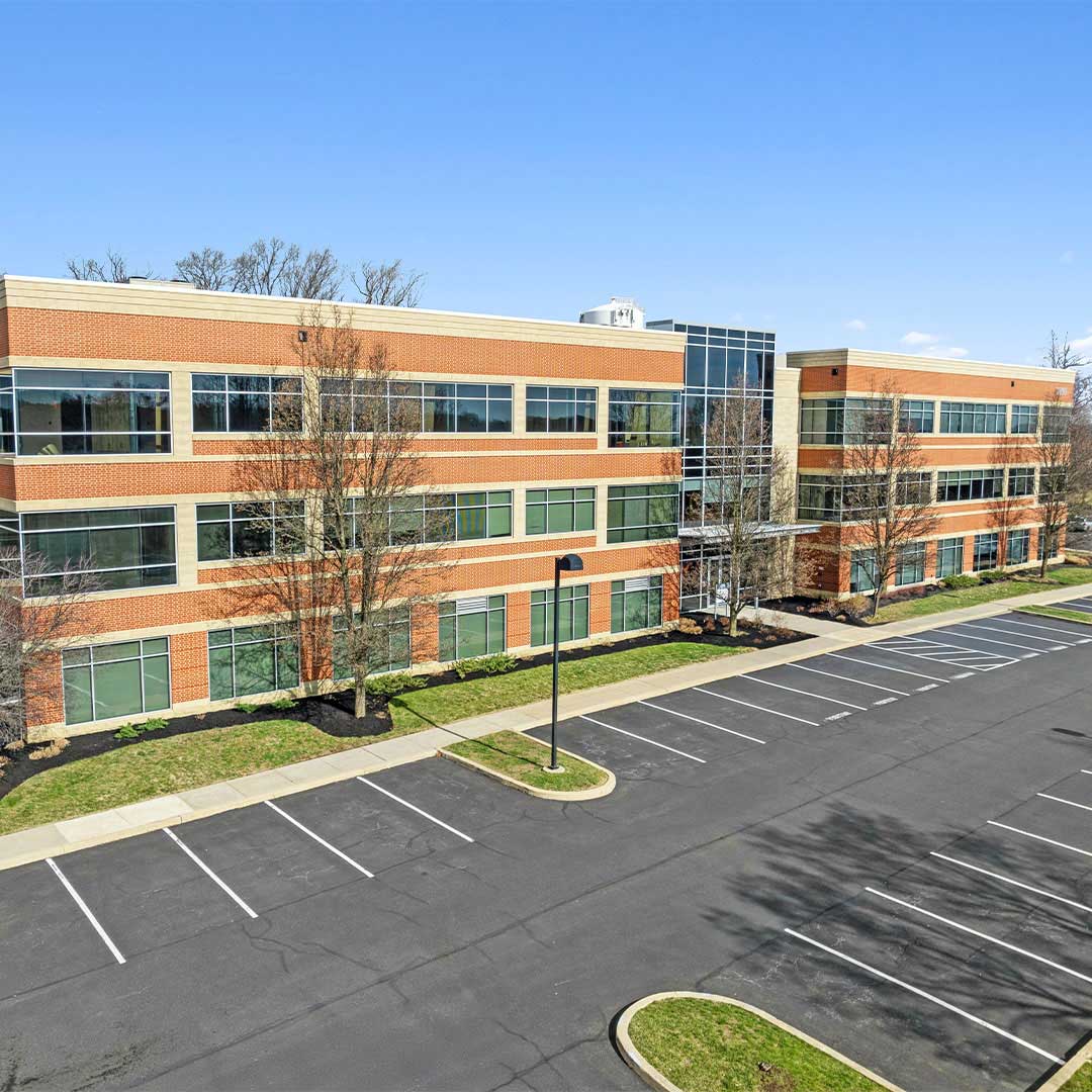 Aerial view of Stone Manor office building featuring a three-story brick exterior, glass windows, and on-site parking in a suburban business park.