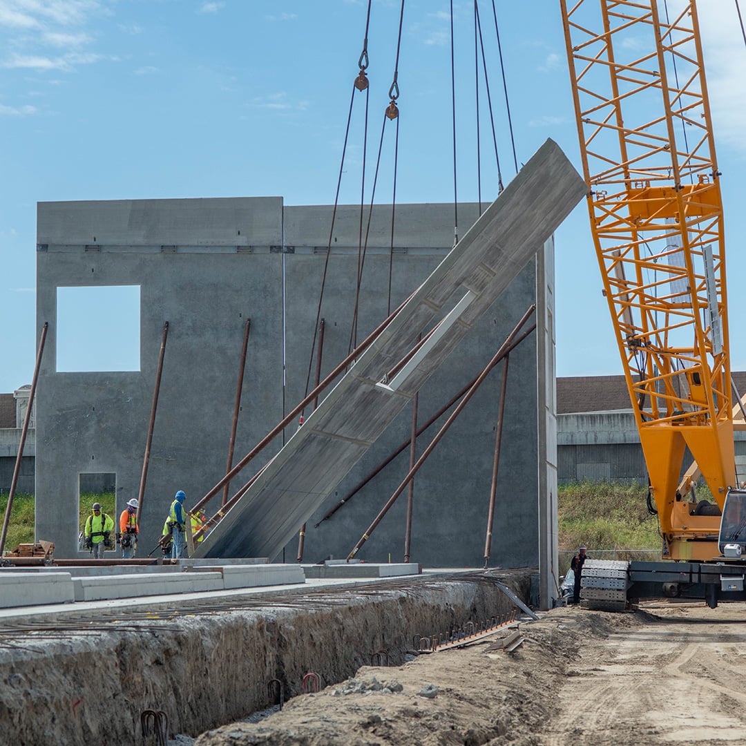 Construction crew using a crane to tilt up a concrete wall panel at an industrial development site.