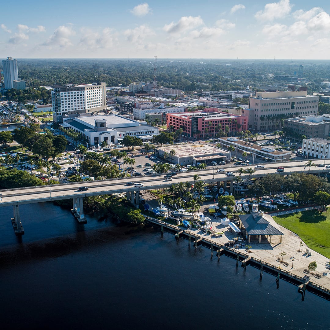 Aerial view of downtown Fort Myers waterfront showing office buildings, marina, bridge, and surrounding urban commercial district.