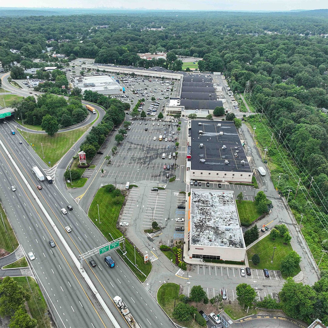Aerial view of Interstate Shopping Center in Ramsey, New Jersey, featuring a large retail strip center with expansive surface parking lots situated alongside a major highway interchange.
