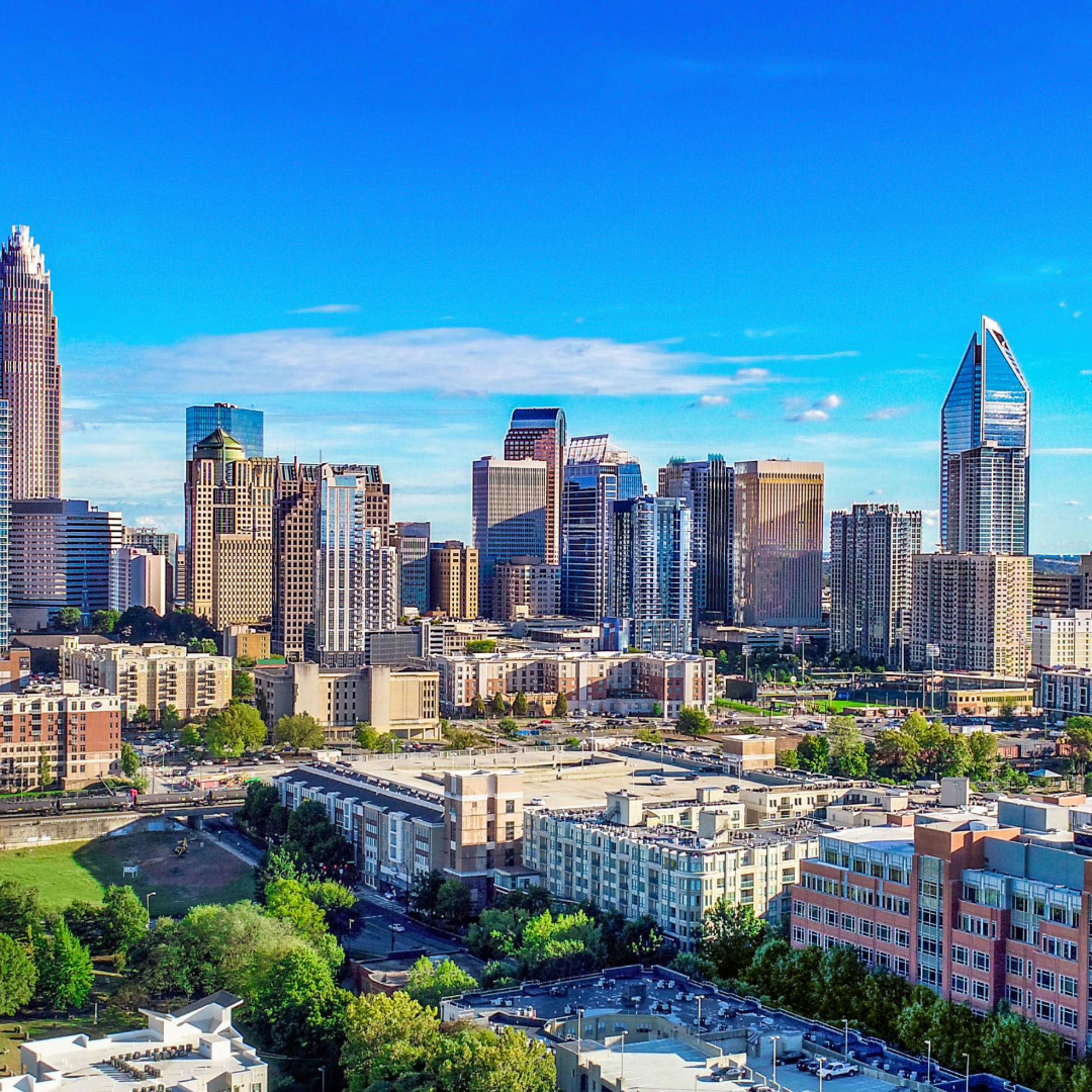 Aerial view of Charlotte, NC downtown skyline with modern skyscrapers, green trees, and blue sky