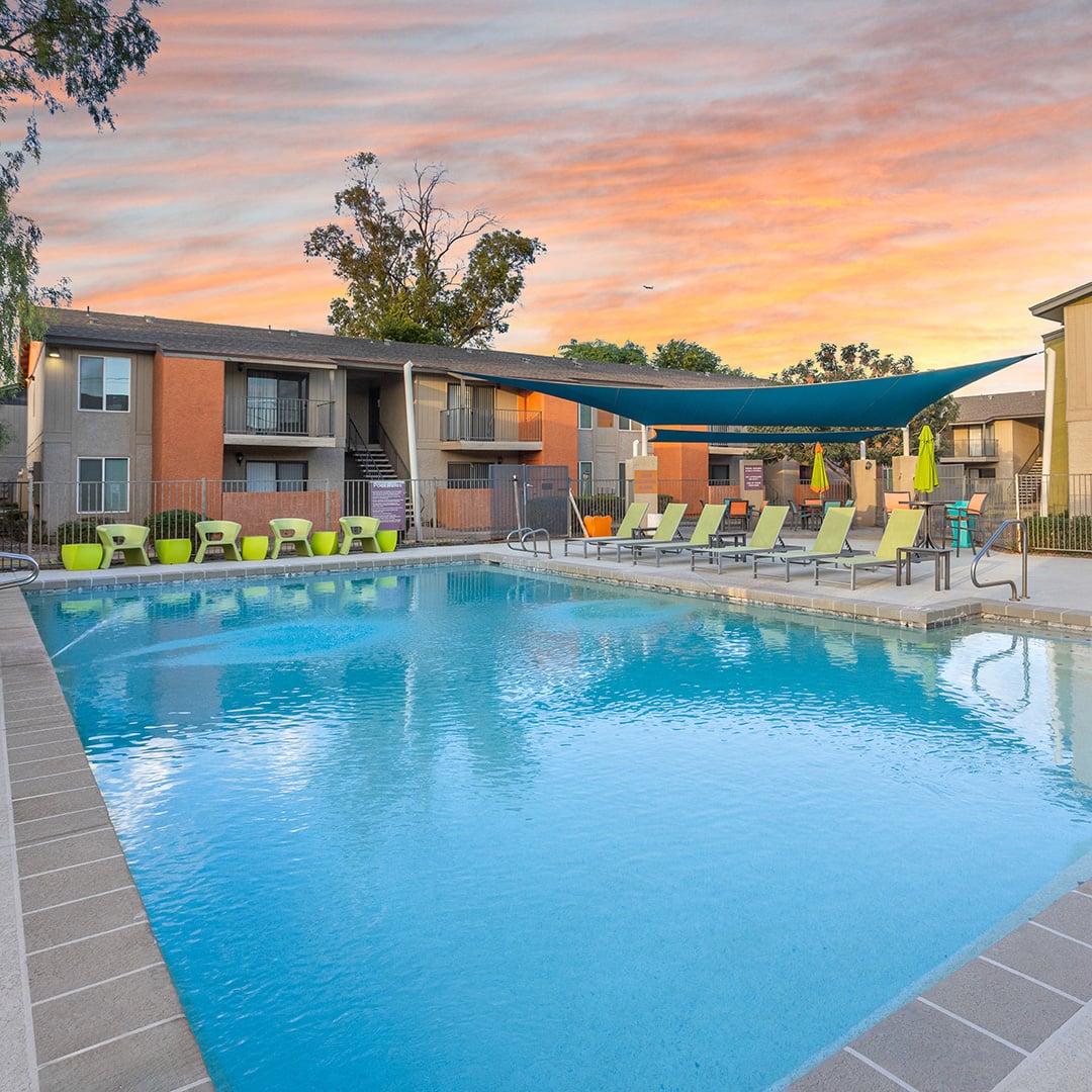 Resort-style pool with lounge chairs and shade sail at Avia multifamily apartment community in Phoenix, AZ at sunset.
