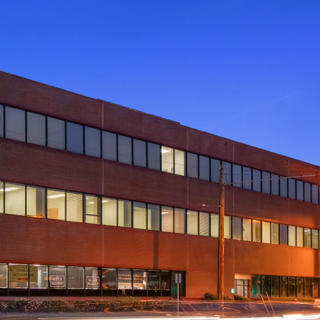 55 E California Blvd, Pasadena CA – three-story brick office building with illuminated windows at dusk, ground-floor retail tenants