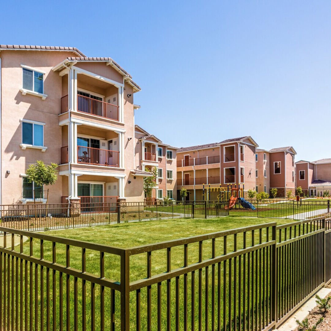 Turtle Creek Apartments exterior with green lawn, iron fence, balconies, and playground in Riverside, CA