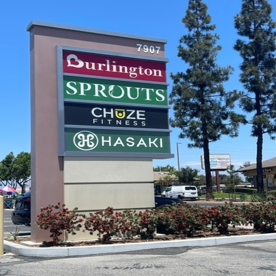 Pylon sign at 7907 displaying Burlington, Sprouts, Chuze Fitness, and Hasaki tenants, surrounded by landscaping and trees.