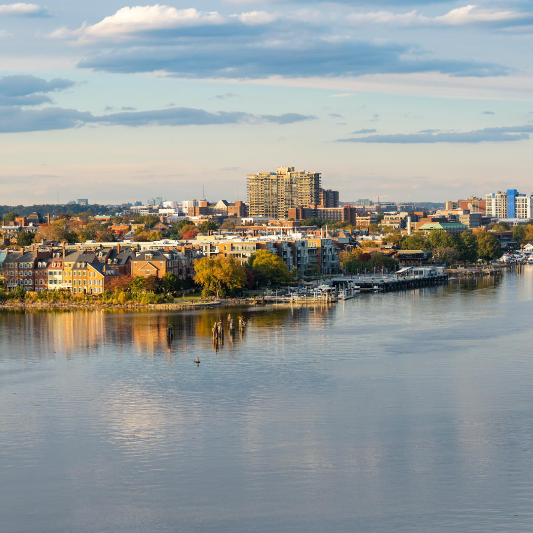 Aerial view of Northern Virginia waterfront skyline with historic buildings, autumn trees, and calm river reflection