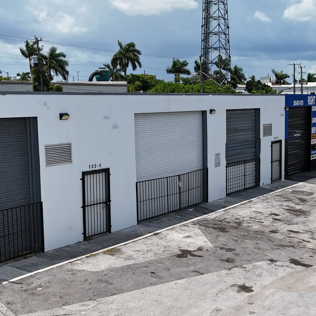 Exterior of a multi-tenant industrial warehouse building with roll-up loading doors and gated access.