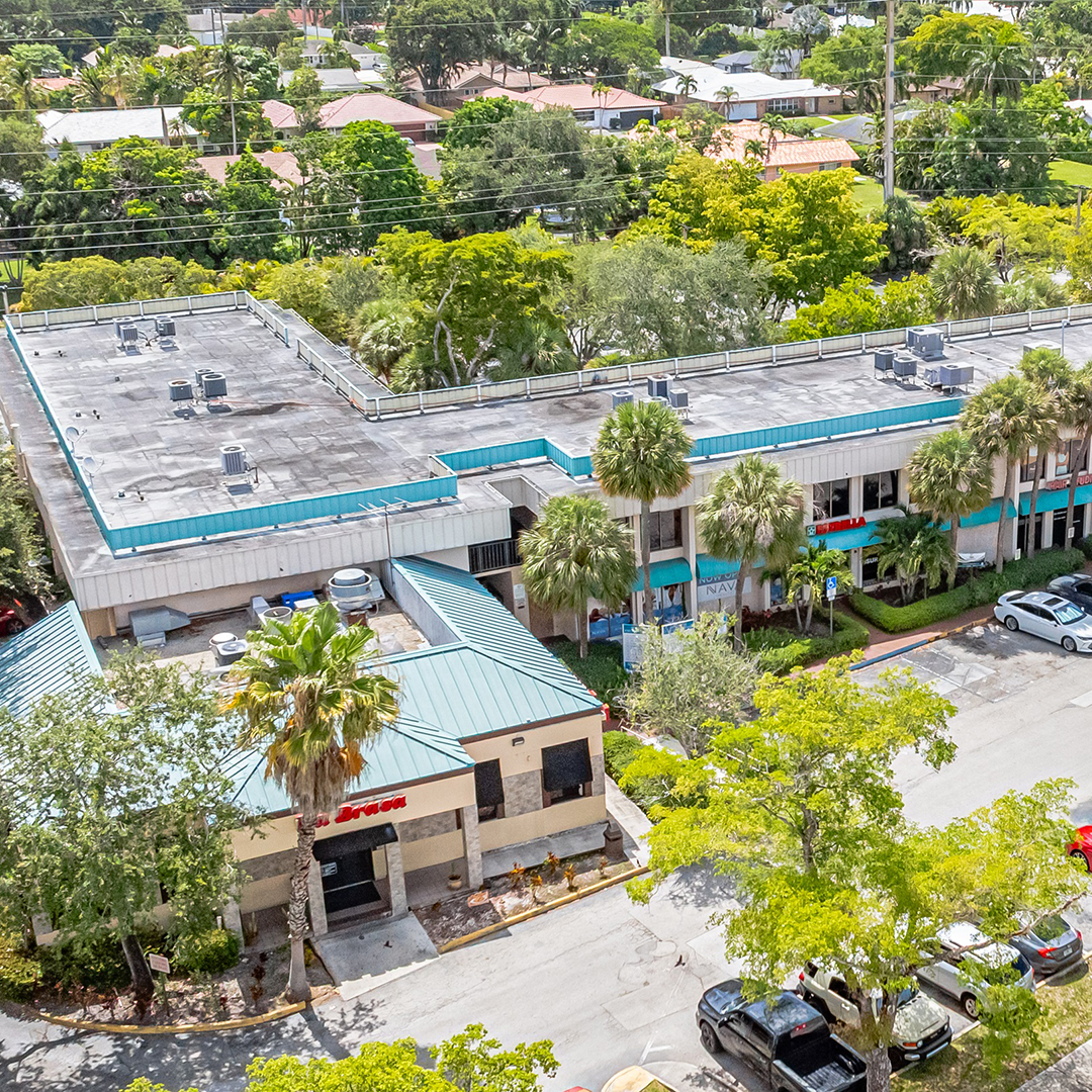 Aerial view of a commercial building surrounded by palm trees and greenery in Plantation, Florida.