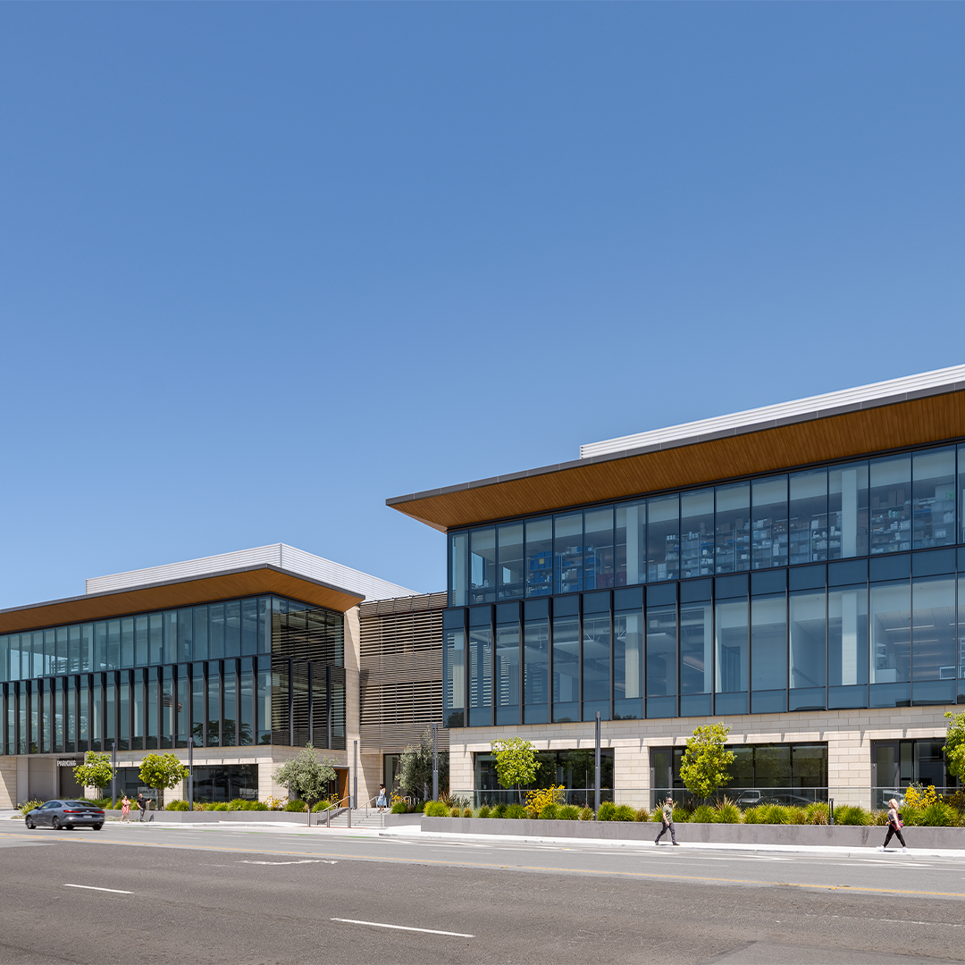 Modern glass‑front office building on Industrial Road in San Carlos, California, shown on a clear day with pedestrians and landscaped surroundings