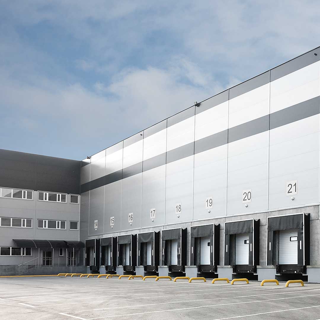 Exterior view of a modern industrial warehouse with multiple loading dock doors numbered 13 to 21.