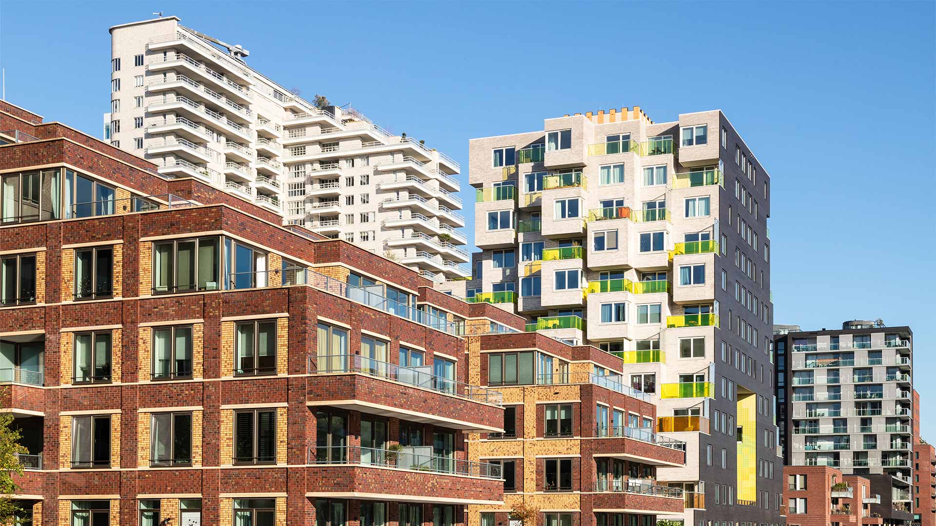 Modern apartment complexes on the waterfront in Amsterdam with striking architecture, brick facades, and colorful balconies under a clear blue sky.