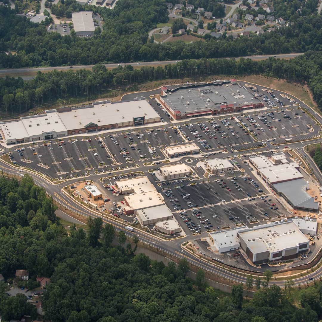 Aerial view of 5th Street Station, a large open-air retail shopping center surrounded by wooded areas, featuring multiple anchor stores and expansive parking lots.